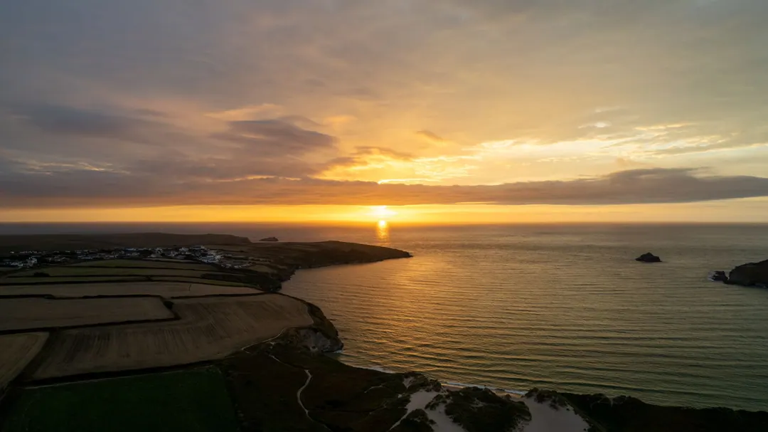 The sun setting into the sea beyond fields and headlands on the Cornish coast