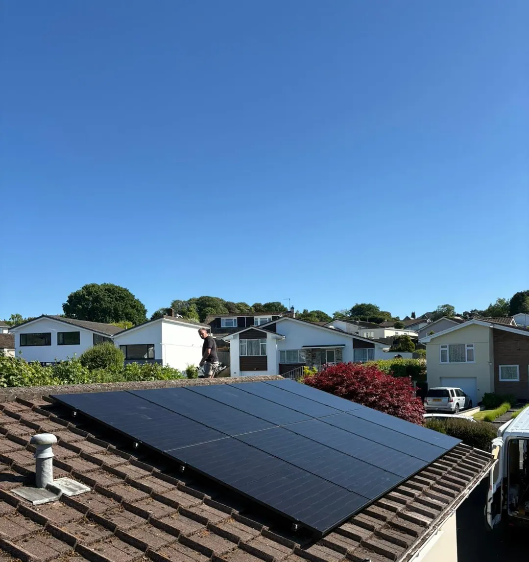 A finished all-black array on a bungalow’s tiled roof, with an installer at the far edge of the roof